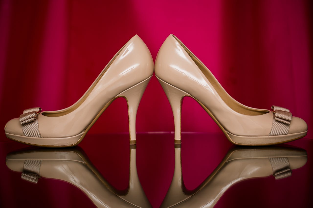 Chic nude high heels with bows, mirrored against a vibrant red background for glamour.