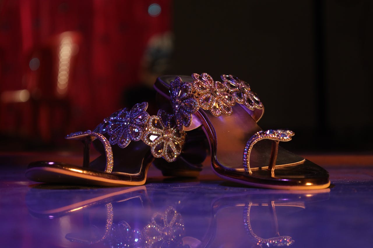 Close-up of elegant jeweled high heel sandals on reflective surface with a dark background.