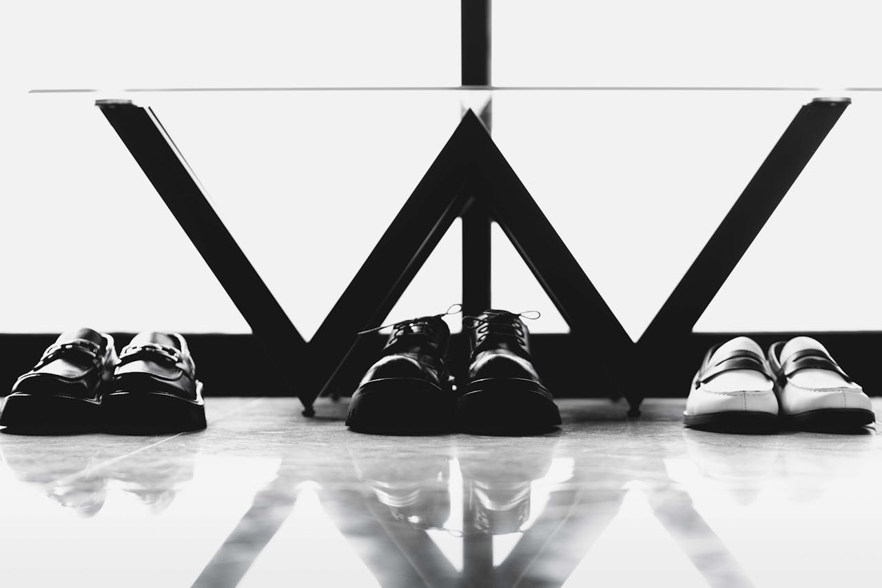 Black and white photo of formal shoes arranged under a modern table, emphasizing style and order.